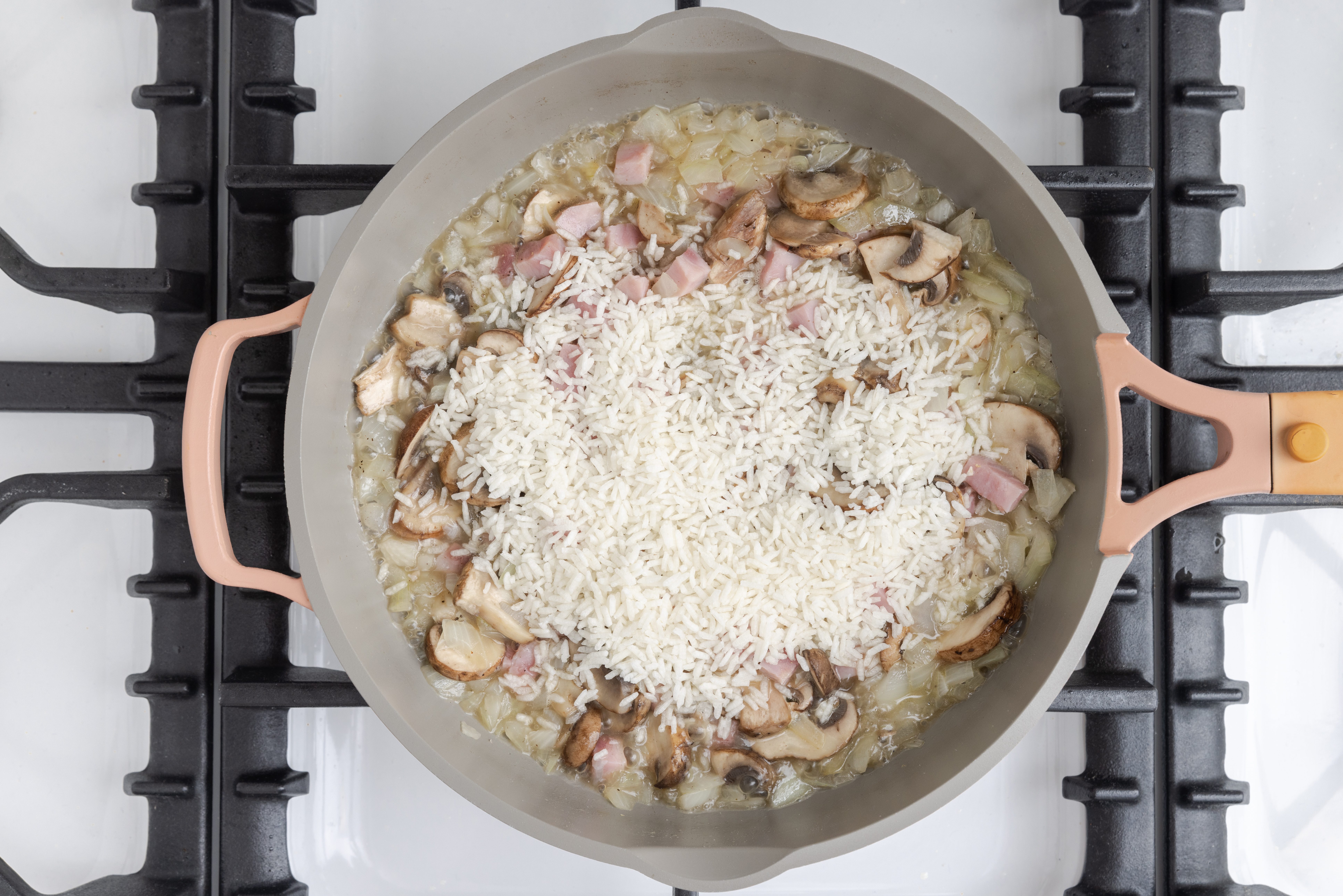 Instant rice and cubbed ham being added to the skillet with mushrooms, onions, chicken broth and water.