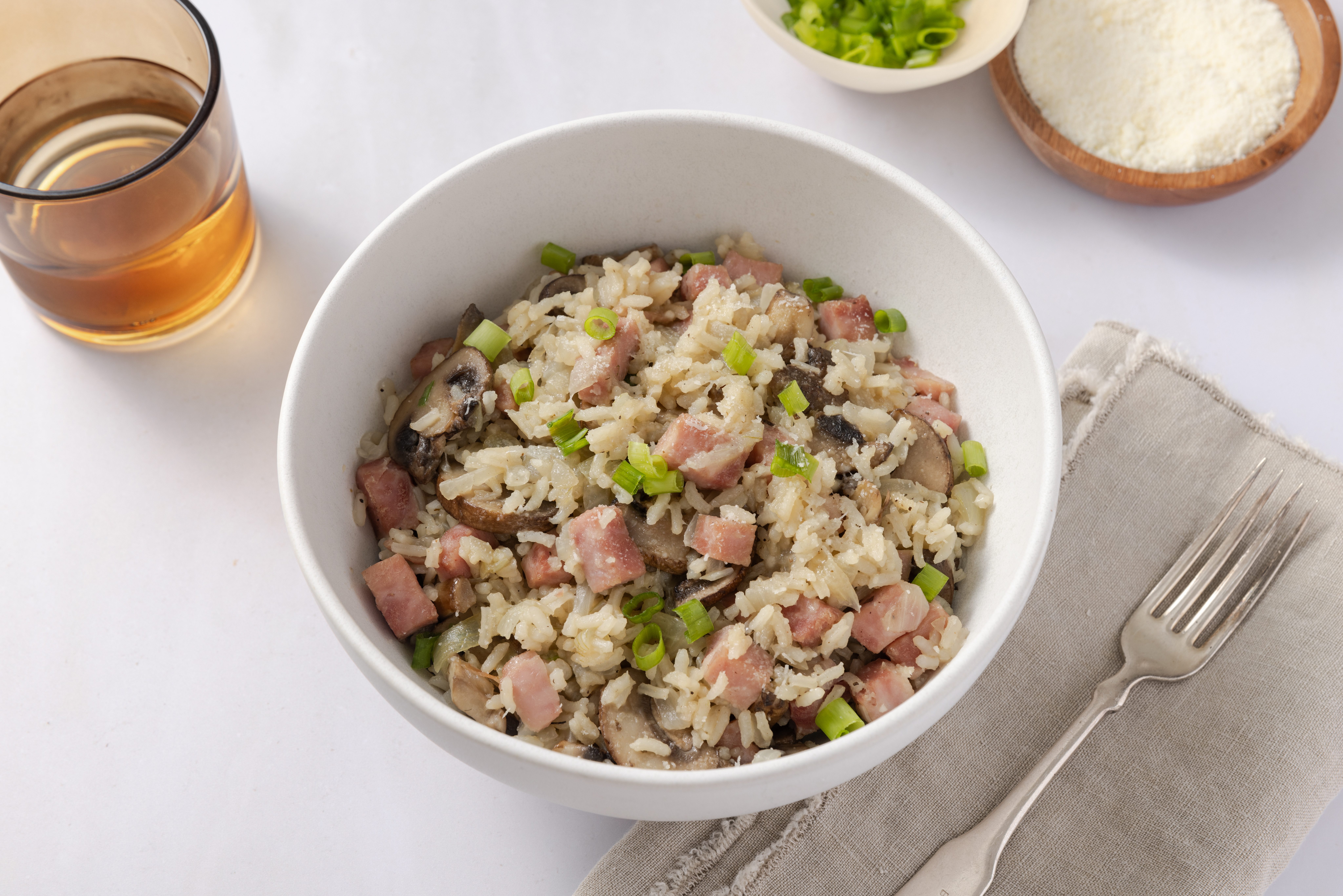 Rice and ham served in bowl, garnished with parmesan cheese and green onions.