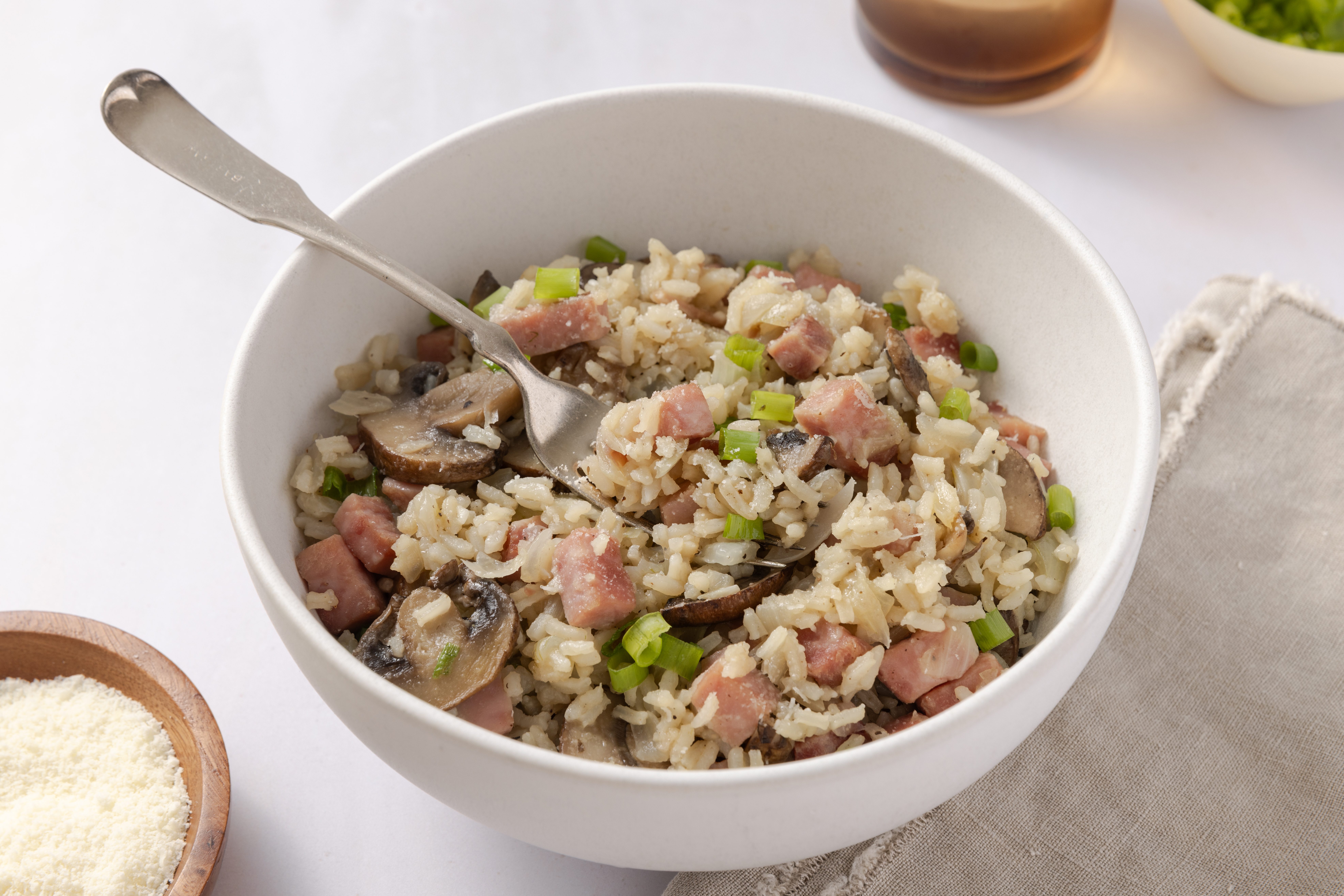 Detail of rice and ham on a fork, garnished with parmesan cheese and green onions.