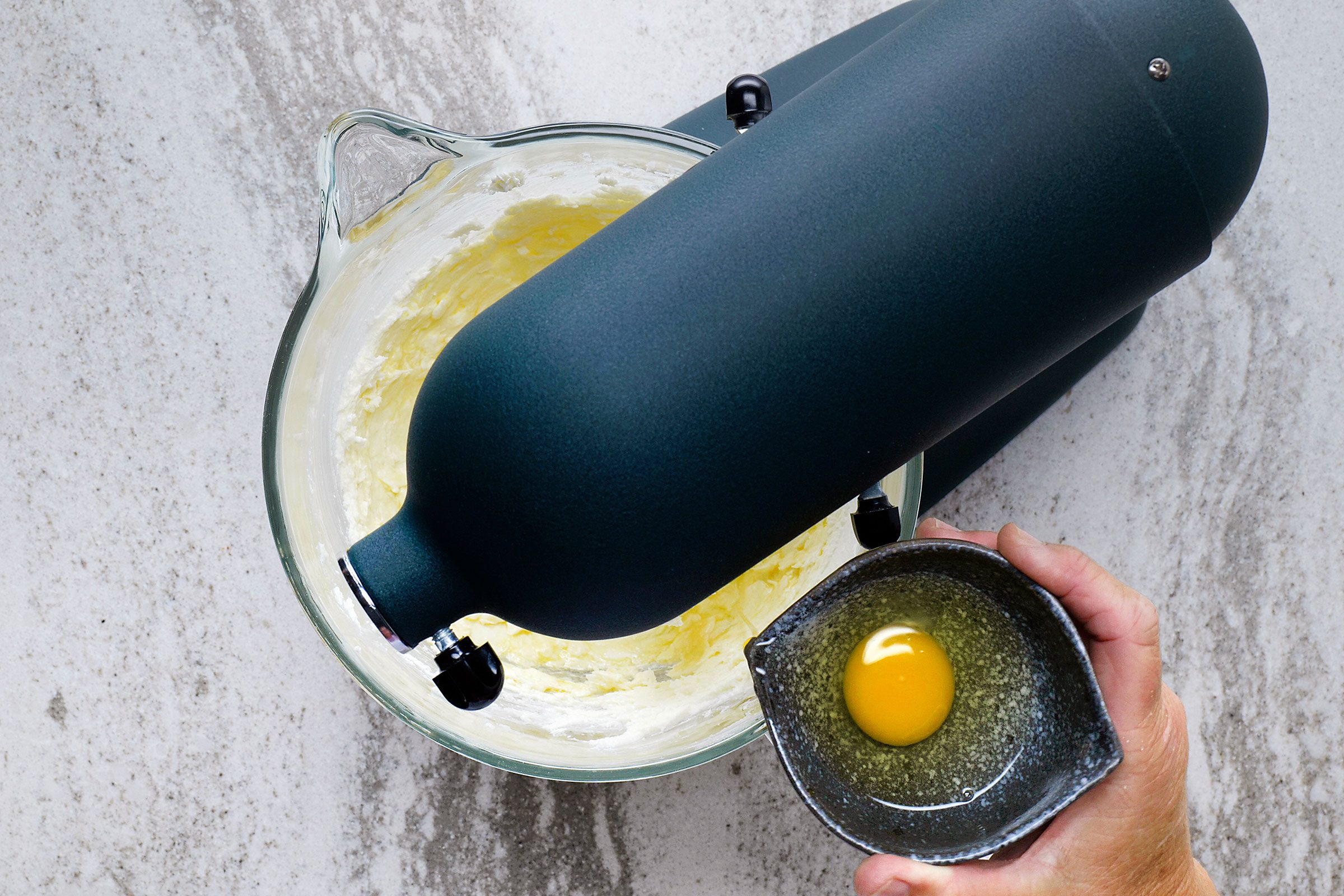 Adding eggs to butter and sugar in a glass bowl