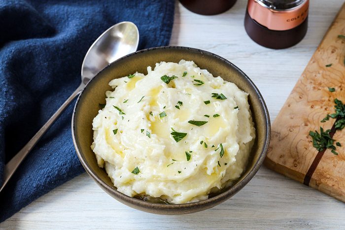 A serving bowl of microwave mashed potatoes with spoon and a bit of chopped parsley.