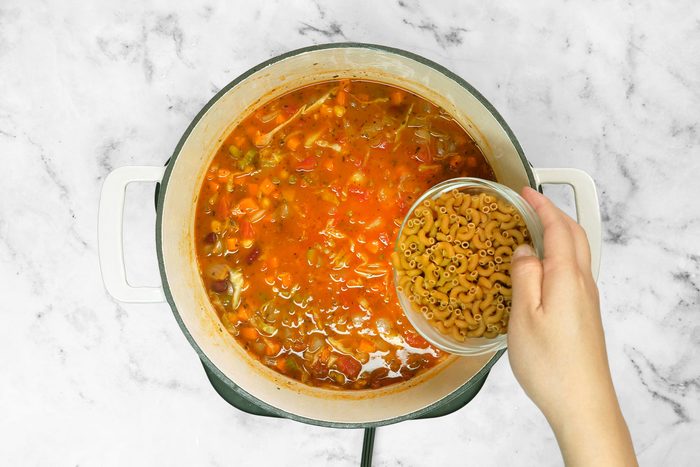 Adding elbow pasta to vegetables and broth mix
