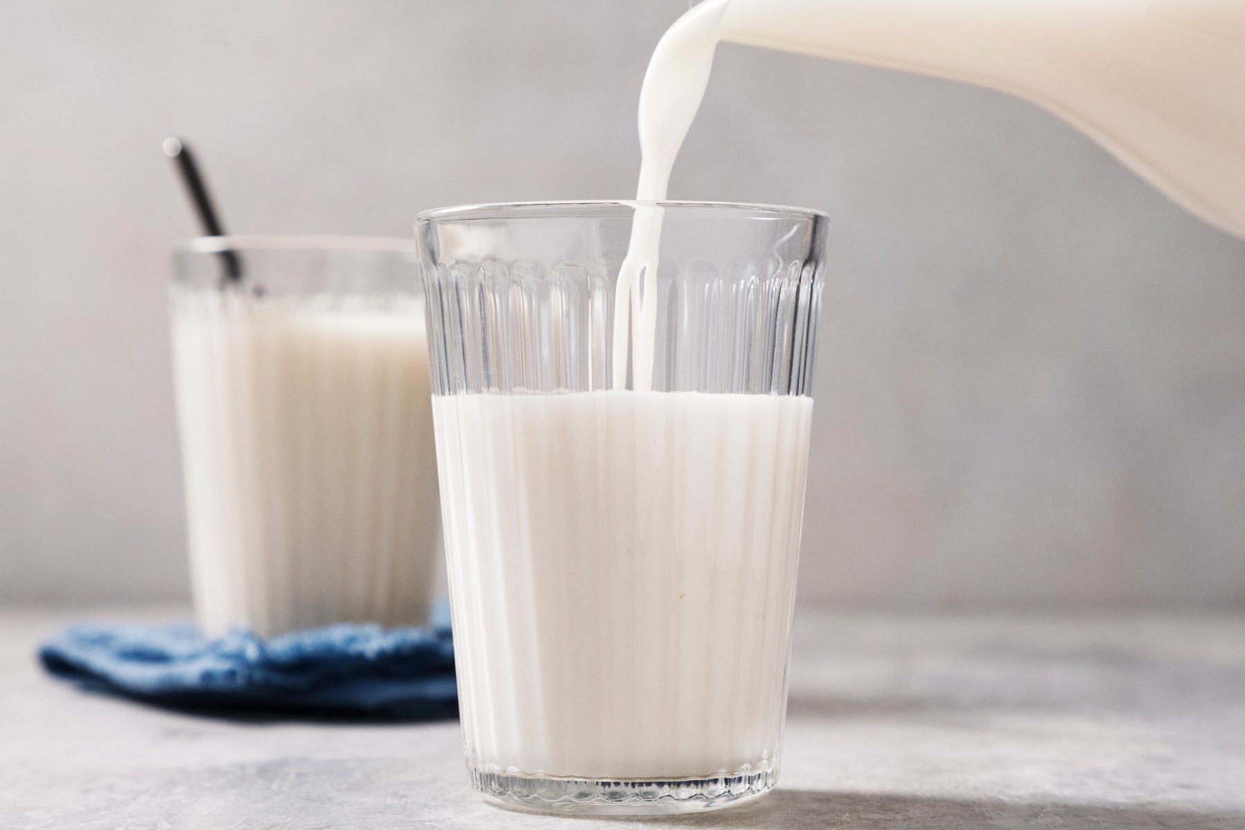 A glass being filled with Oat Milk from a glass jug.