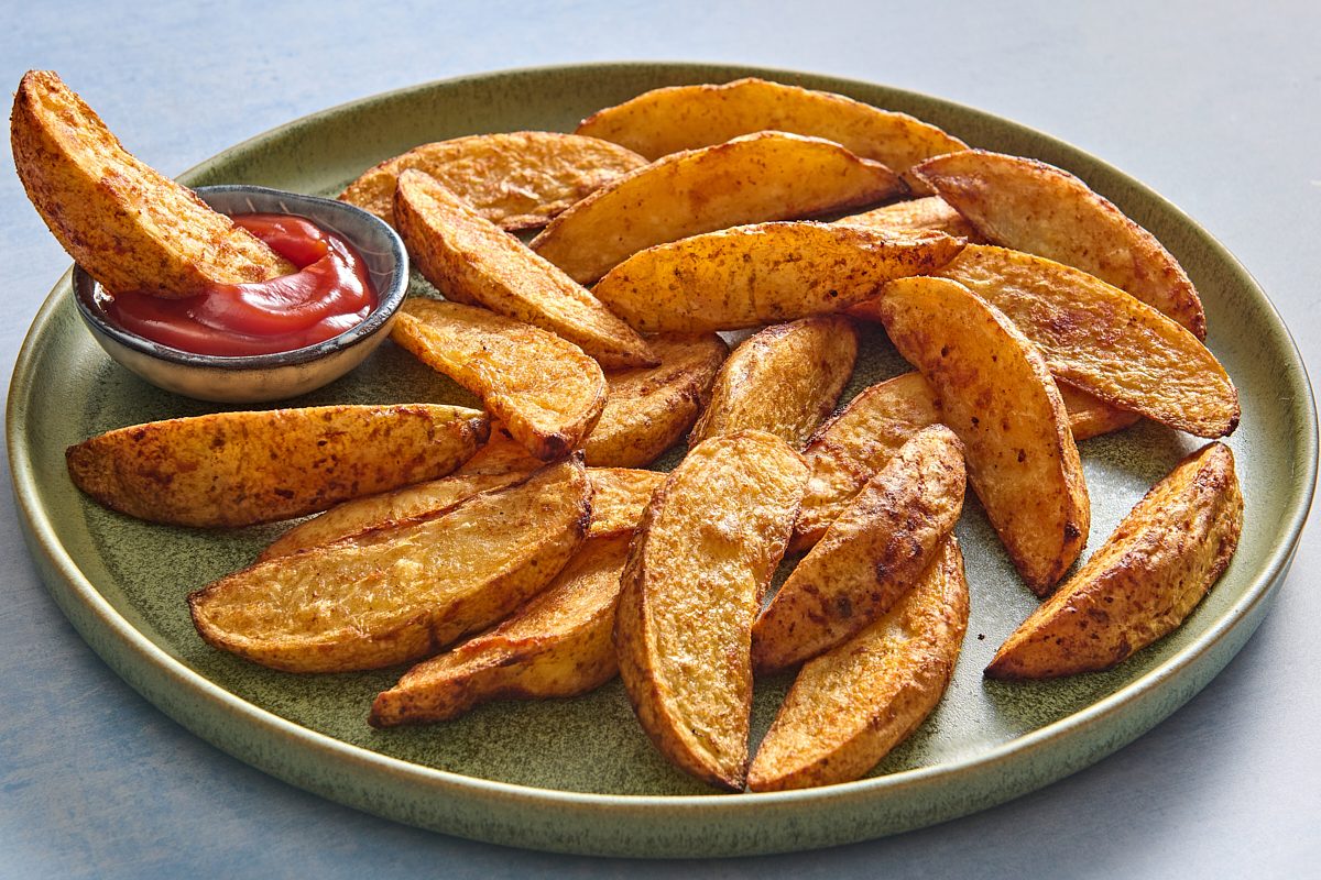 Closeup of a plate of oven fries, with one being dipped into some ketchup