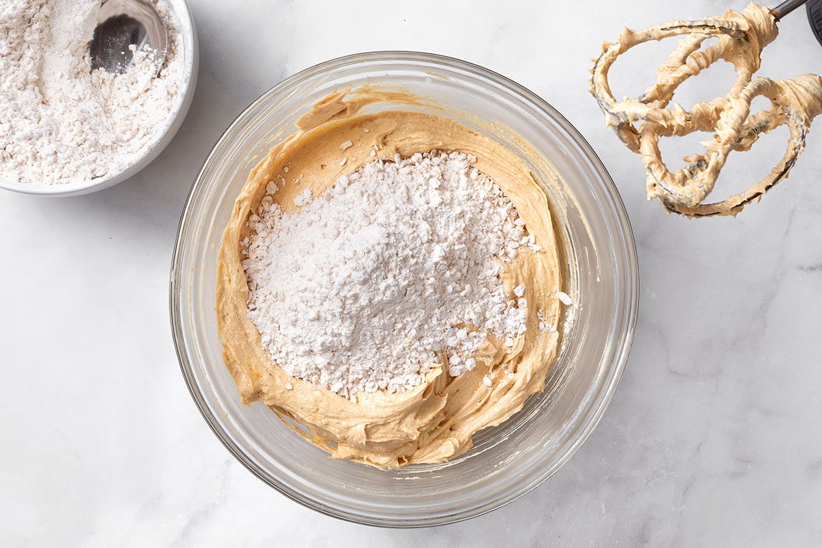 Flour, oats, baking soda and salt mixture added to a bowl of whipped sugars, peanut butter, eggs, vanilla and water in a mixture bowl for step one of Peanut Butter Cookie Bar for Taste of Home