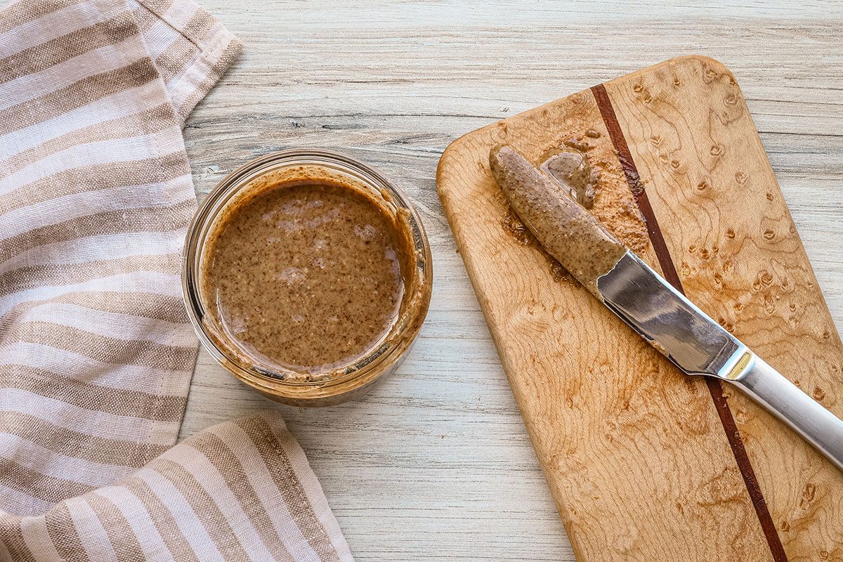 An overhead photo of pecan butter in a jar with a knife for spreading.