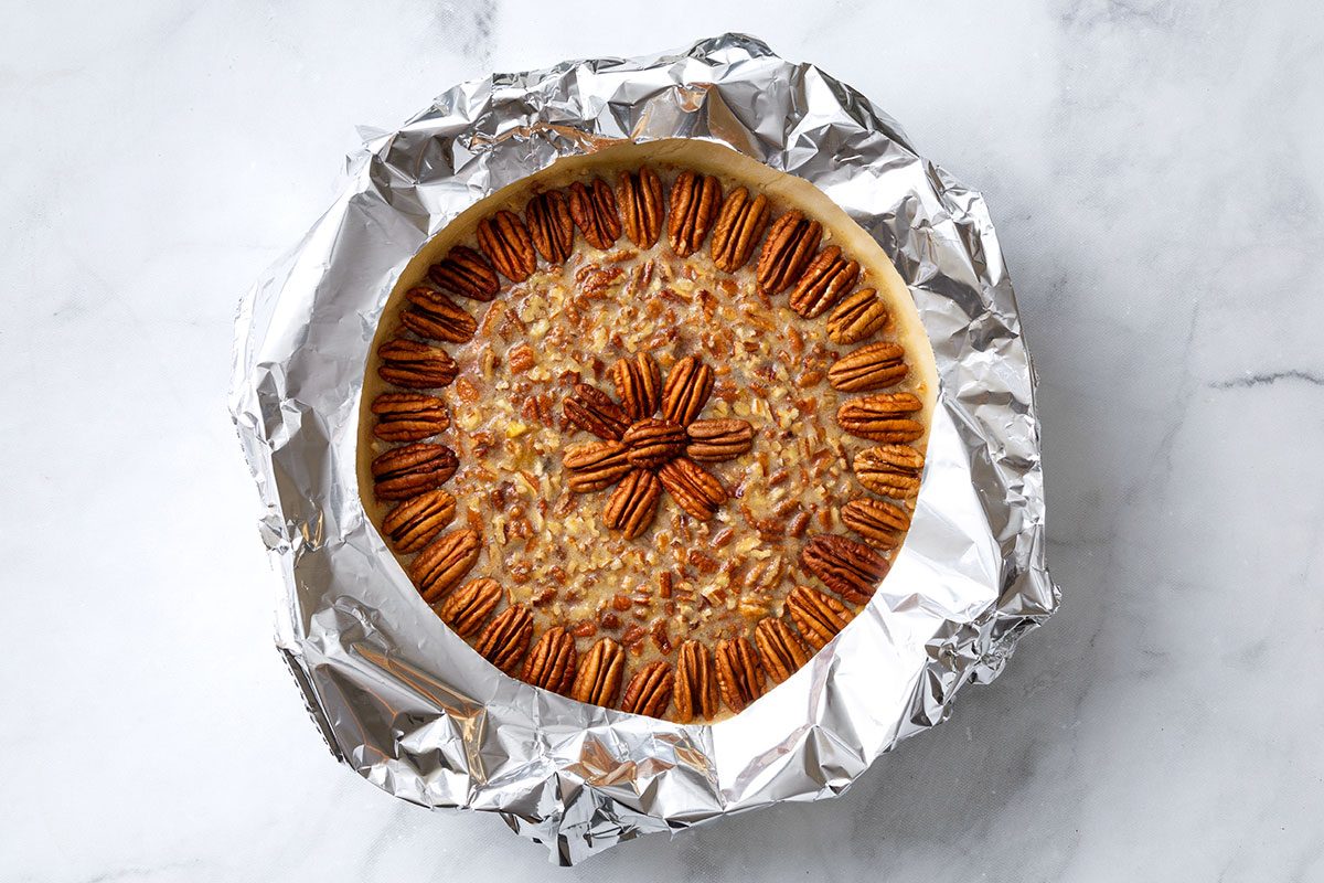 Pie crust with pecan filling topped with pecan halves and crust wrapped with foil for step three for Pecan Pie without Corn Syrup for Taste of Home