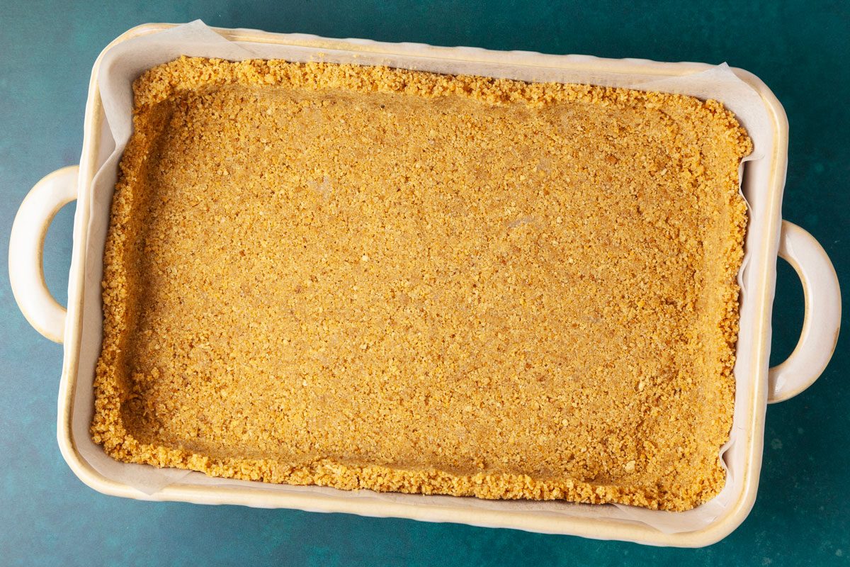 Step 1 of Taste of Home Pecan Pie Cheesecake Bars is to grease and line an 11 x 7 inch baking dish with parchment paper. In a large bowl, combine the crushed graham crackers, sugar and melted butter. Press into the bottom of the baking dish until it’s about 1-inch thick. Bake until just browned, approximately six to eight minutes. Remove and cool to room temperature