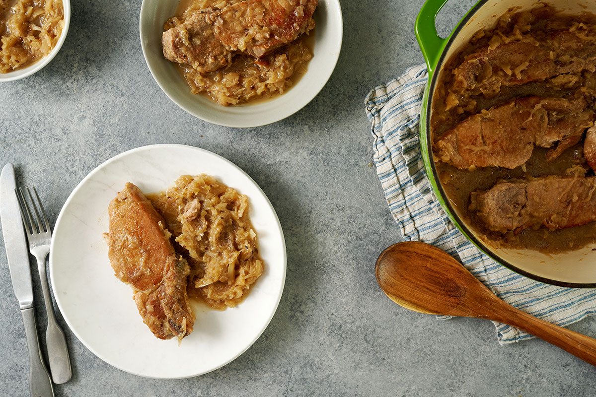 Overhead hero shot of the finished Taste of Home Pork and Sauerkraut, showcasing the tender pork ribs and sauerkraut mixture served on a plate and next to Dutch oven.