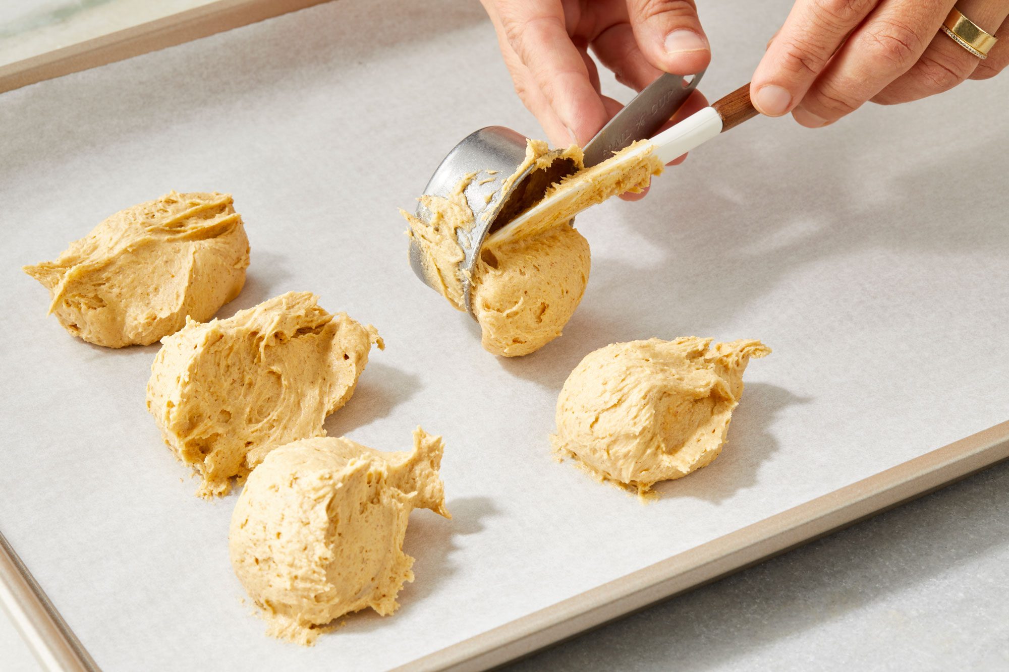 Quarter cupfuls of finished cookie dough scoops on parchment lined baking sheet