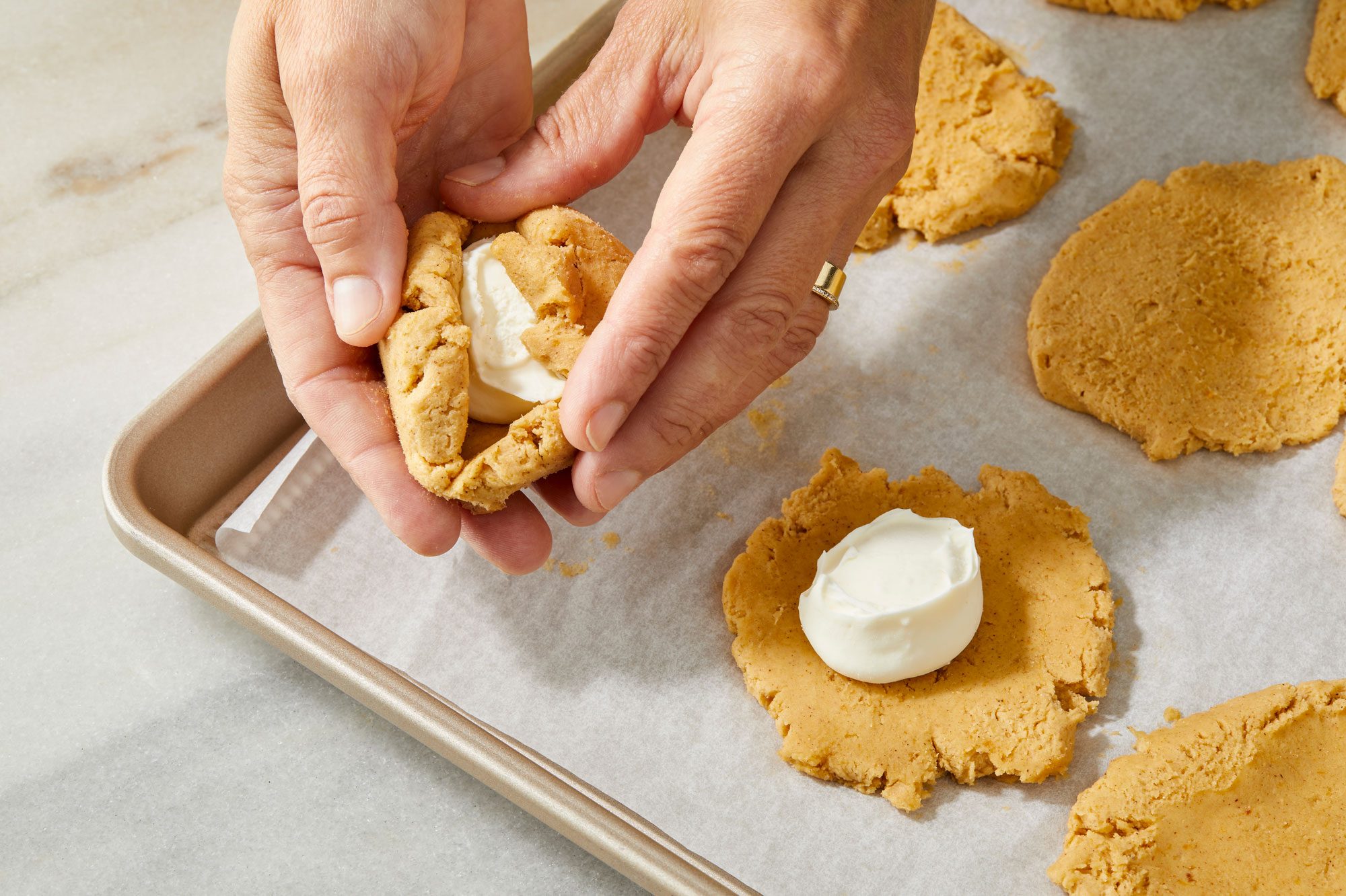 CU of hand wrapping dough over cream cheese scoop with a frozen cream cheese scoop on the flattened ones