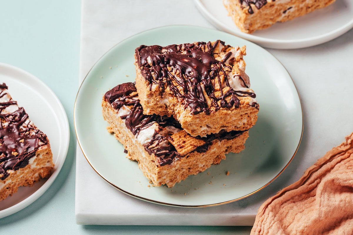 Square Smores Bars stacked on a small plate on a marble board, one bar with a missing bite, recipe by Taste of Home