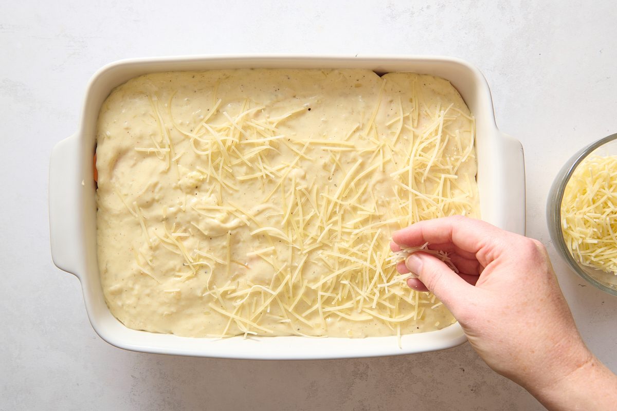 Sprinkling gruyere cheese over the sweet potatoes covered in sauce before baking