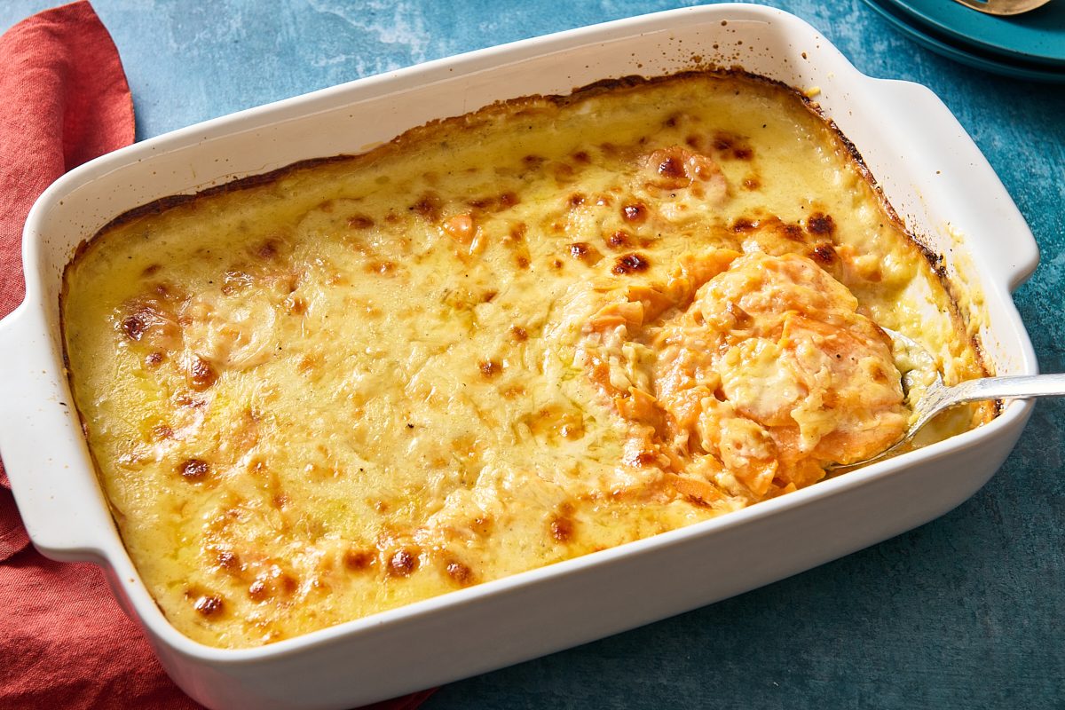 Shot of a baking dish filled with baked scalloped sweet potatoes actively being scooped out