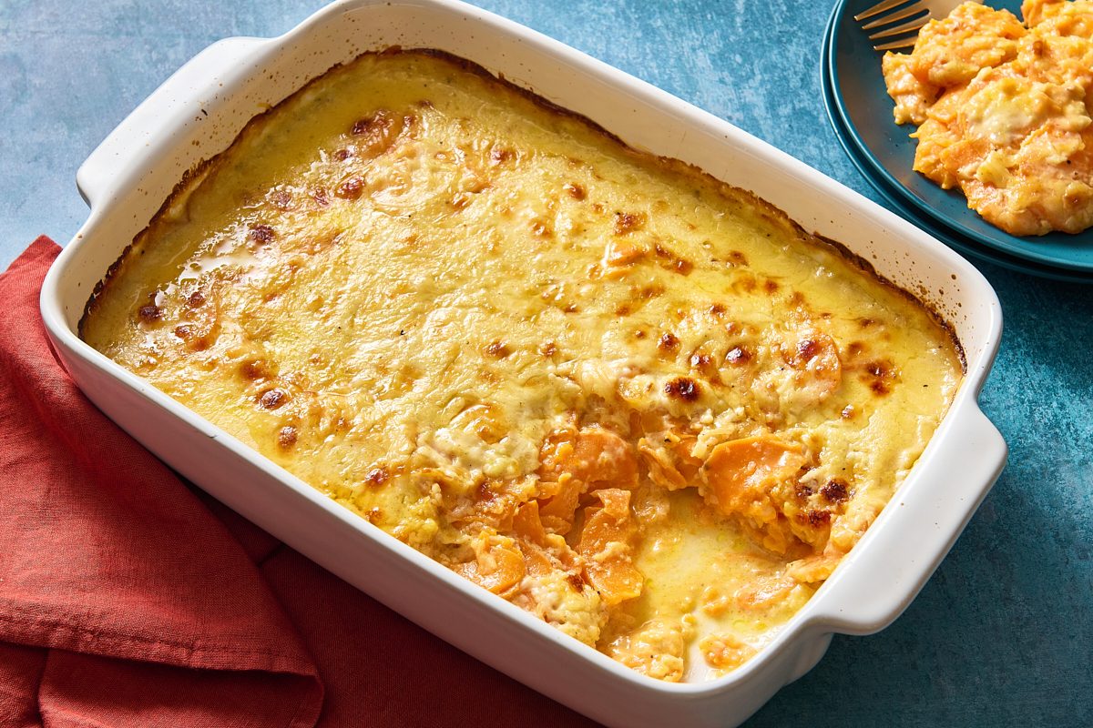 Scalloped sweet potatoes in a baking dish with a portion removed, with a plated portion in the background
