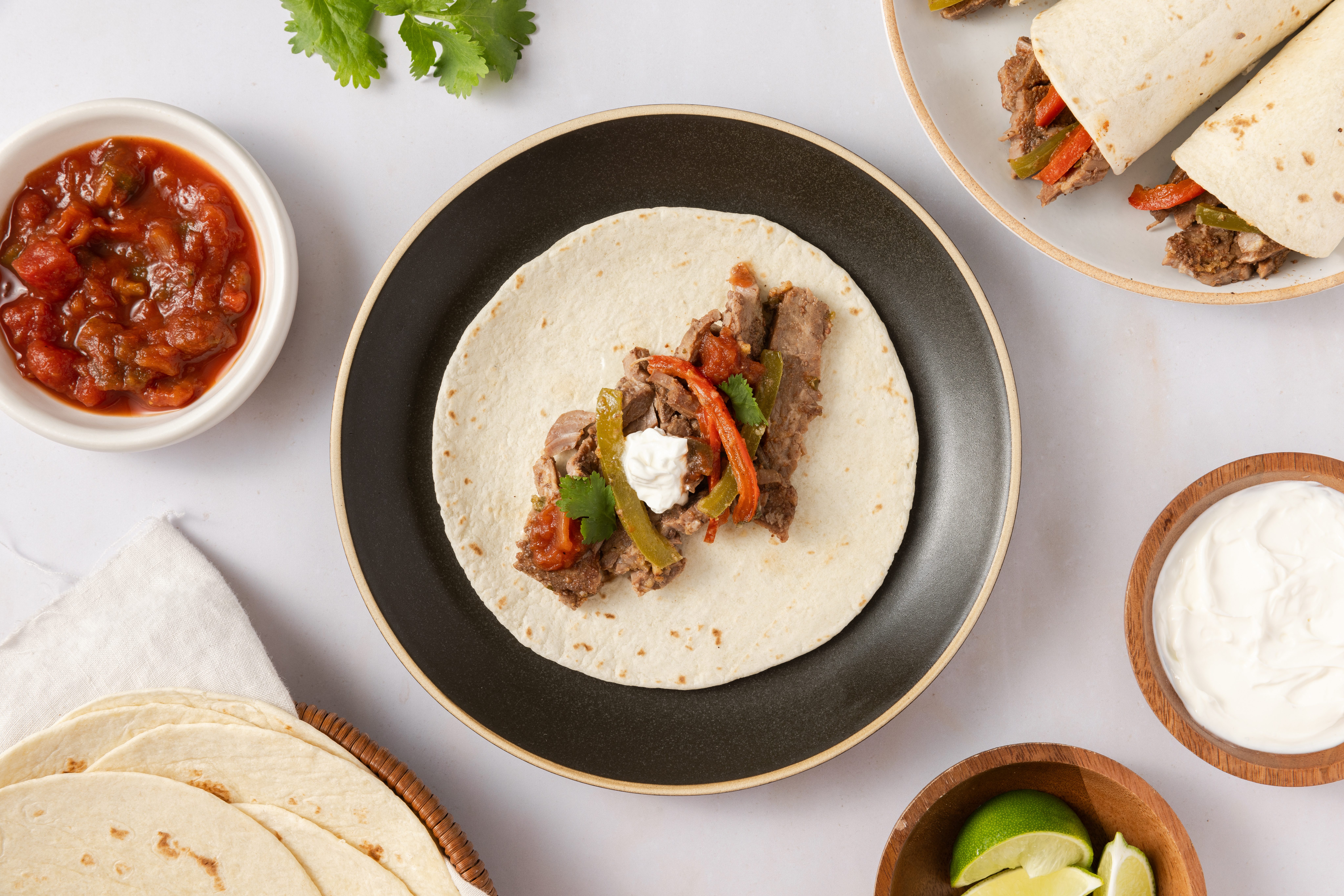 Fajitas ready on plate with folded fajitas in the background.