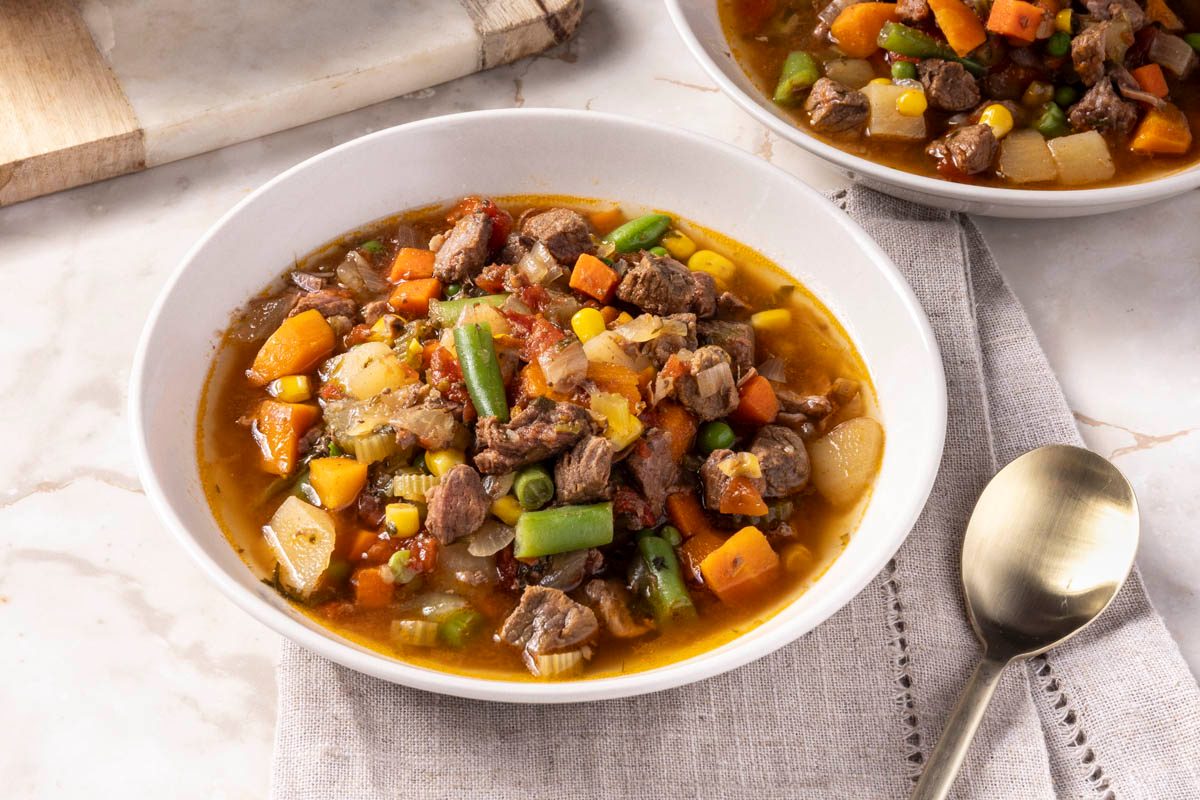 Slow Cooker Vegetable Soup in a white bowl next to cutting board and spoon