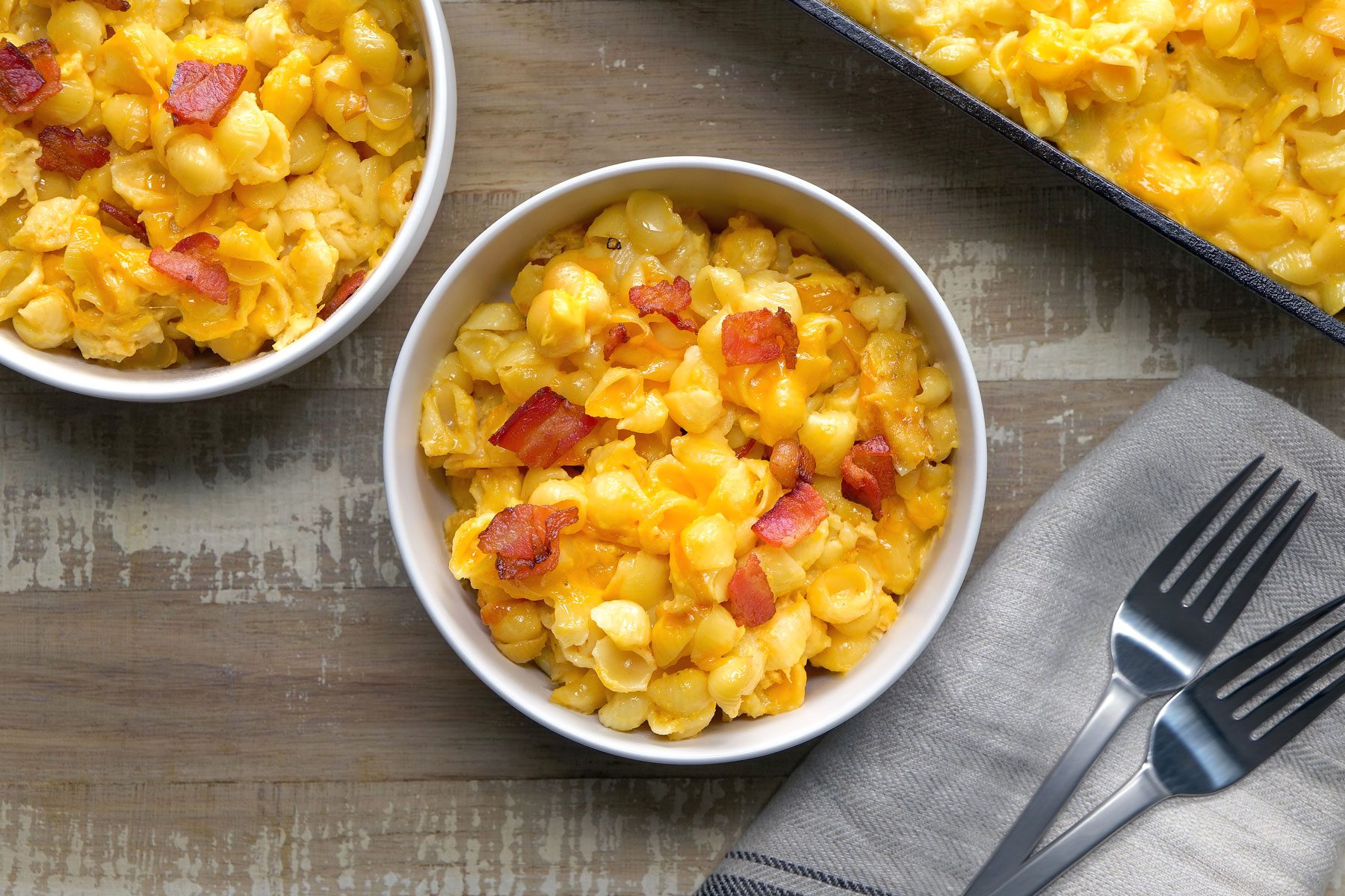 Smoked Mac And Cheese in a bowl with 2 forks next to it. Another bowl and a pan are visible at the corners.