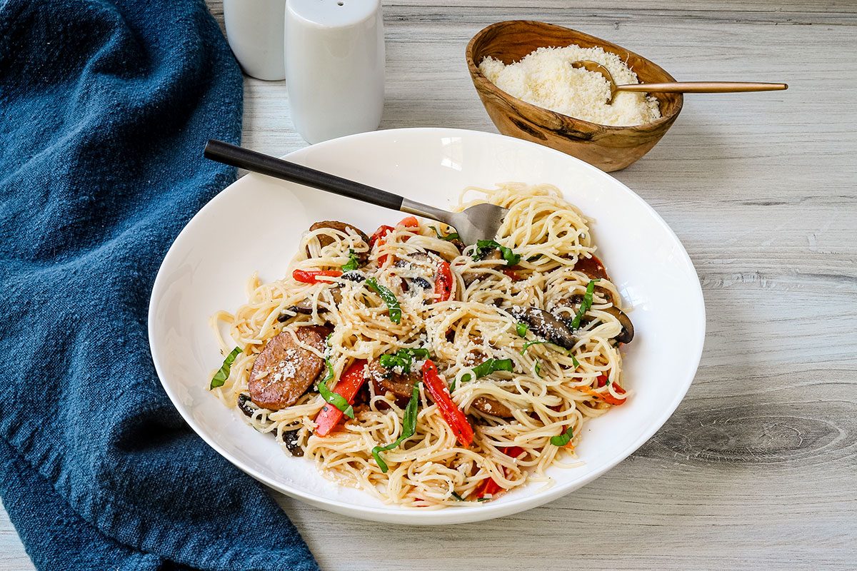 Smoked sausage and pasta meal plated in a pasta bowl with Parmesan cheese on the side.
