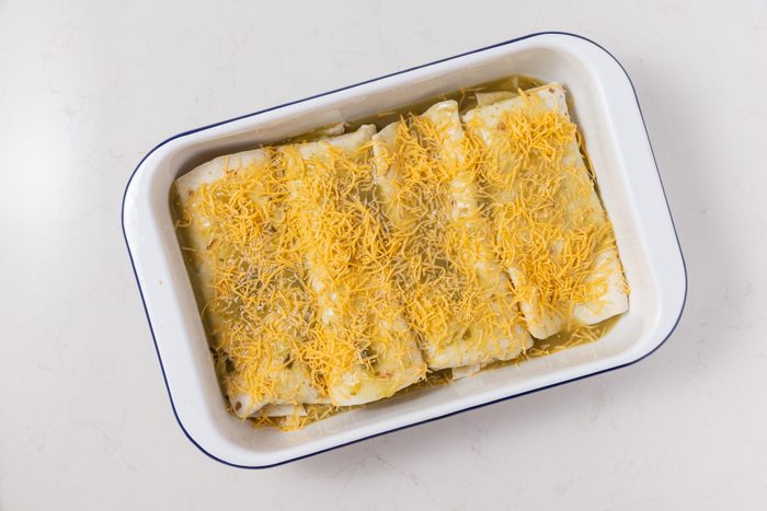 Smothered burritos in baking dish, topped with shredded cheddar cheese.