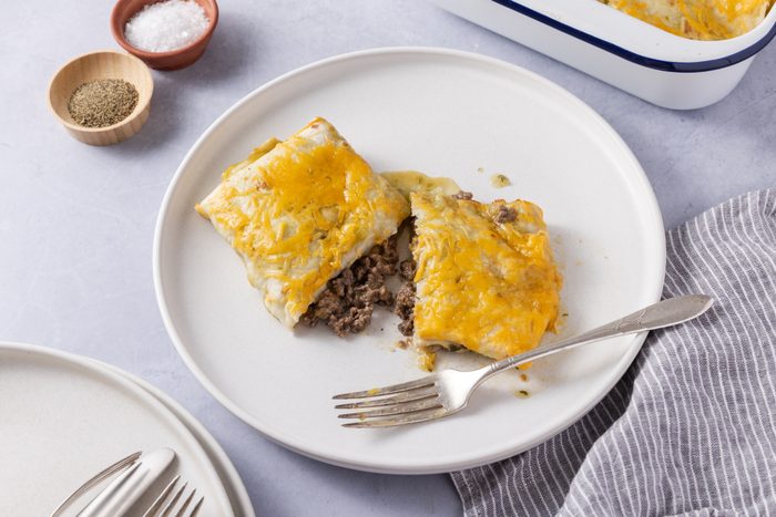 Smothered burrito served on plate, cut in half to show inside, with baking dish in the background.