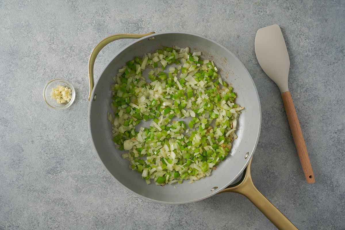 Overhead view of freshly chopped green peppers, onions, and garlic sauteing in olive oil in a nonstick skillet for the Taste of Home Southwest Rice recipe.