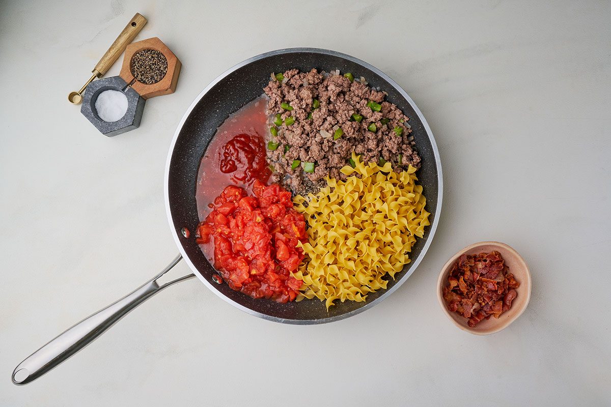 Adding diced tomatoes, chili sauce, and egg noodles to the skillet for Taste of Home's Spanish Noodles recipe