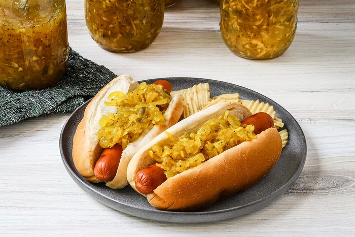 Homemade squash relish on hot dogs with jars in the background.
