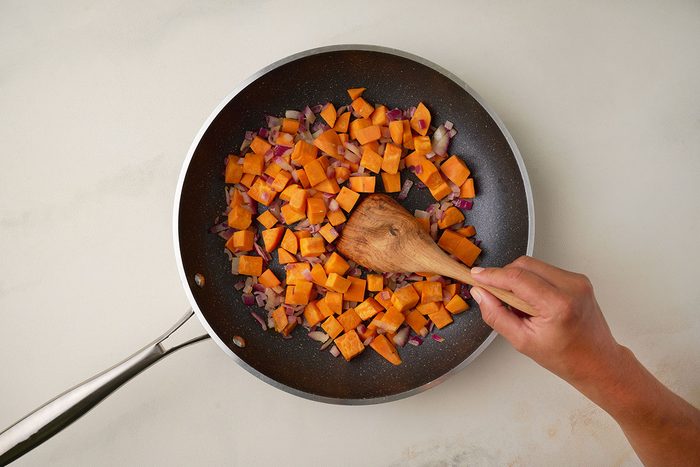 Overhead shot of sautéing sweet potatoes and onions in a skillet for Sweet Potato Bowl.