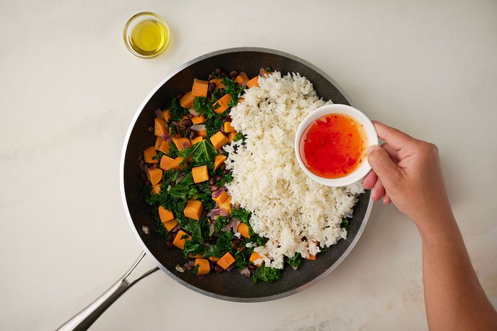 Overhead shot of chili sauce and oil being mixed into the rice in the skillet with other ingredients for Sweet Potato Bowl
