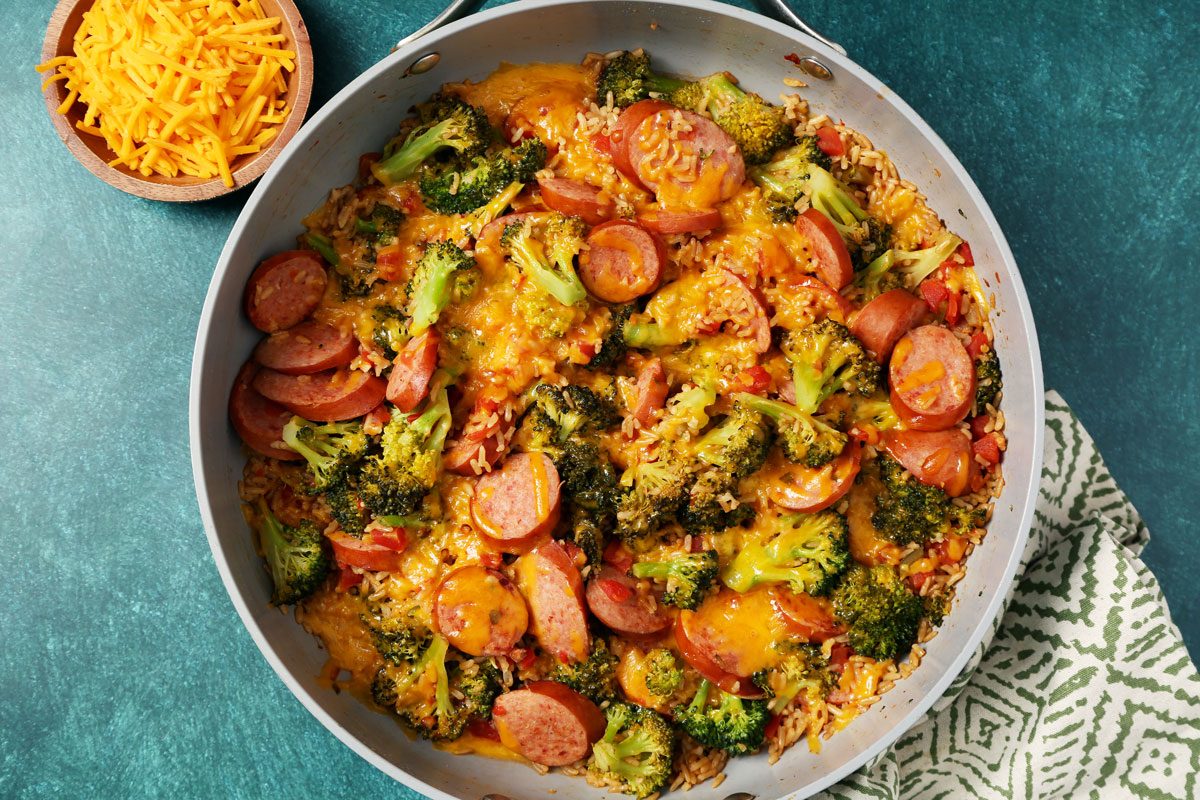 Process of making Taste of Home's Sausage, Rice and Broccoli in a large skillet on a green surface with a green linen.