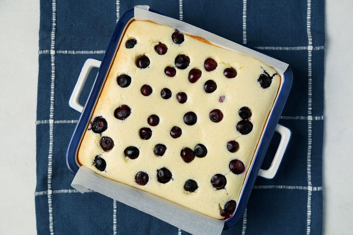 Process of making Taste of Home's Blueberry Cheesecake Bars in a baking dish on a blue linen cloth.