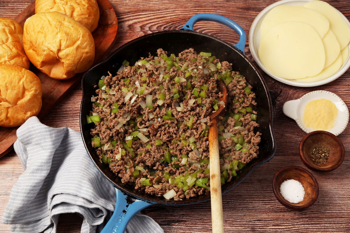 Process of making Taste of Home's Philly Cheesesteak Sloppy Joes on a brown wooden surface. Meat browned in a skillet.