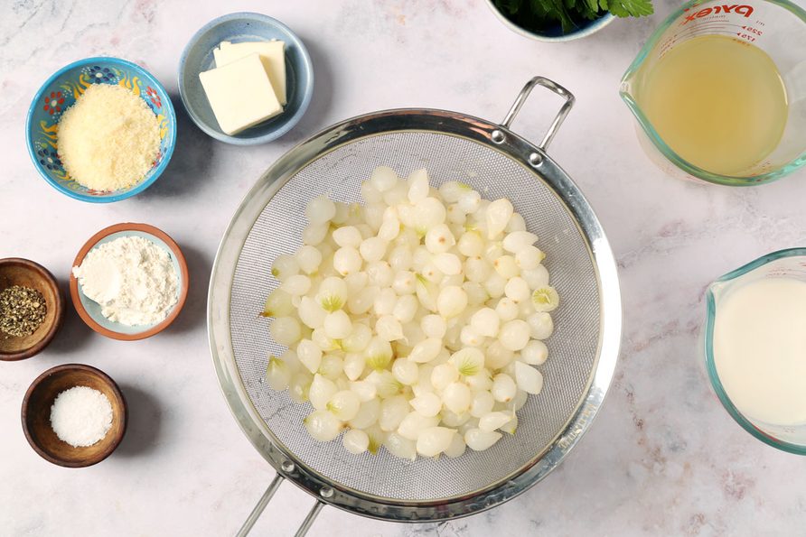 Ingredients for Taste of Home's Creamed Pearl Onions laid out in small bowls on a grey marble surface.