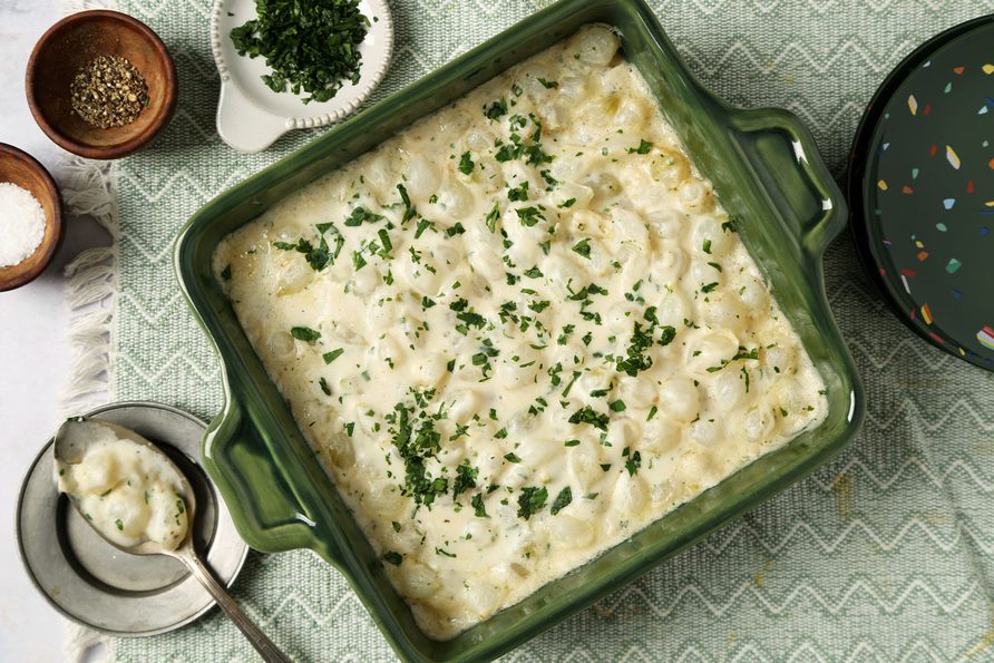Close up of Taste of Home's Creamed Pearl Onions in a green casserole dish on a grey marble surface.