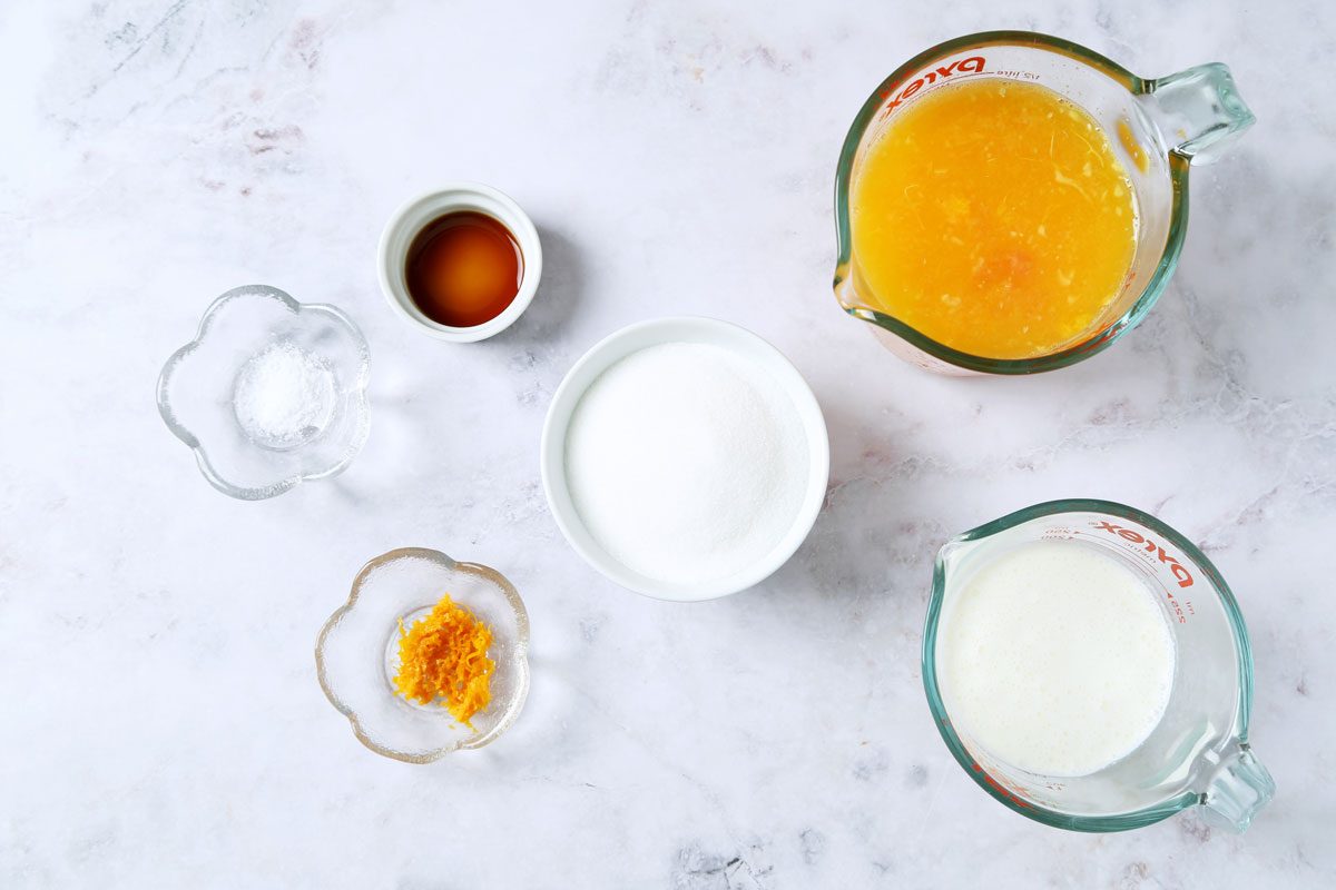 Ingredients for Taste of Home's Orange Sherbet laid out in small bowls on a white marble surface.