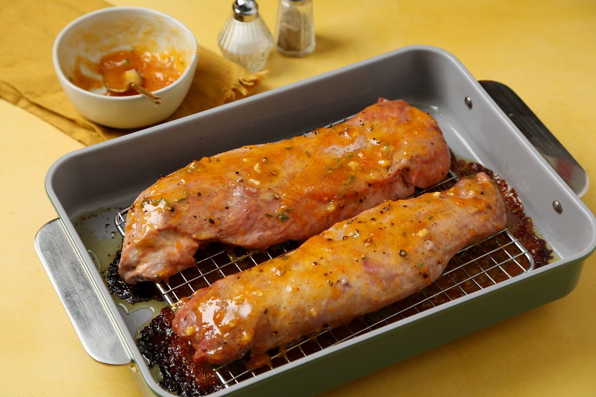Process of making Taste of Home's apricot glazed pork tenderloin roasting on a roasting rack on a yellow surface.