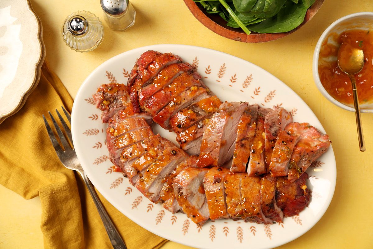 Close up of Taste of Home's apricot glazed pork tenderloin sliced and served on a large plate on a yellow surface.