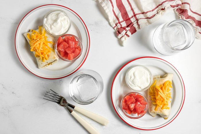 Taste of Home Taco Burrito on enamel plates with bowls of sour cream and tomatoes
