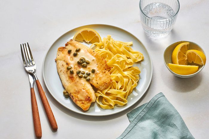 Tilapia fillet served with pasta and lemon butter sauce on a serving plate with a lemon wedge on the side