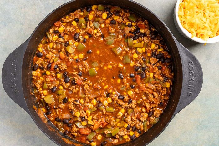 Taste of Home Turkey Black Bean Chili photo of all the ingredients simmered and a side of cheddar cheese for topping.
