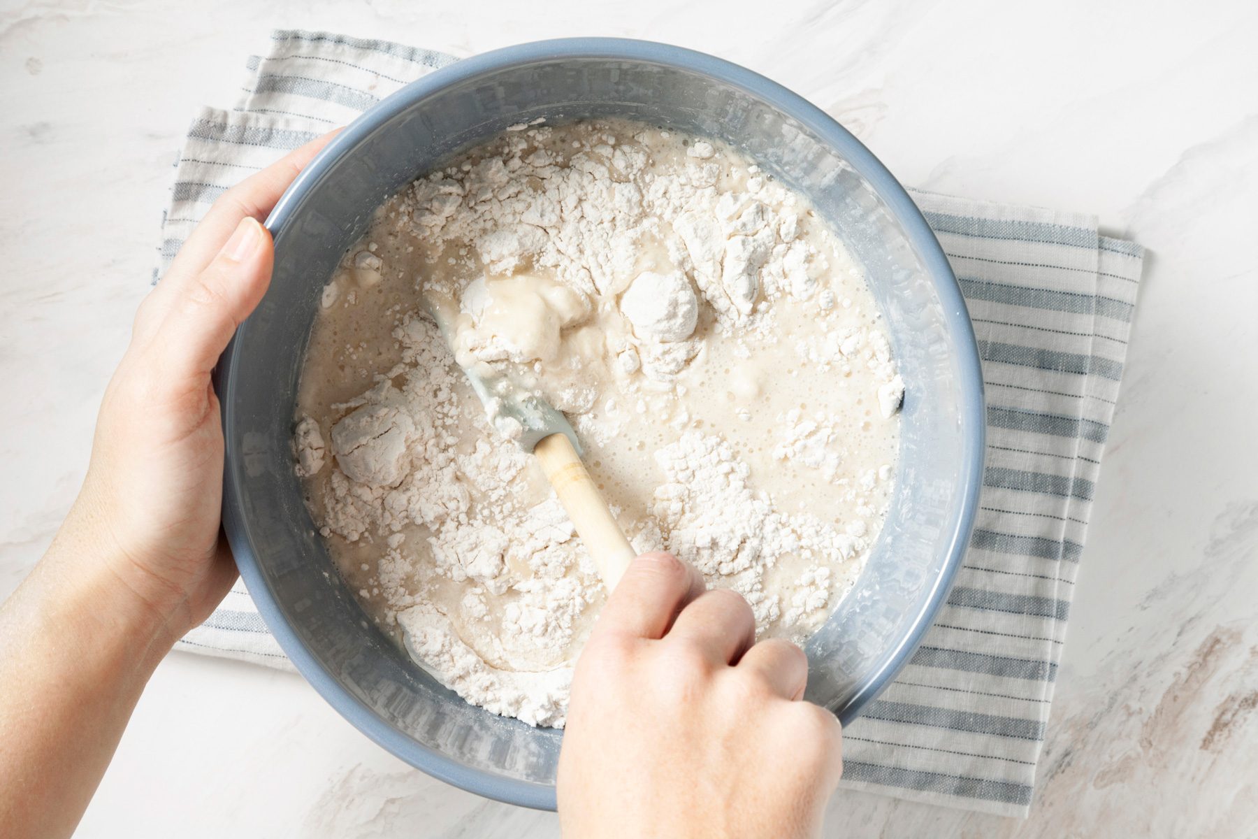 A hand holding a utensil mixes ingredients into the batter for a vegan birthday cake.