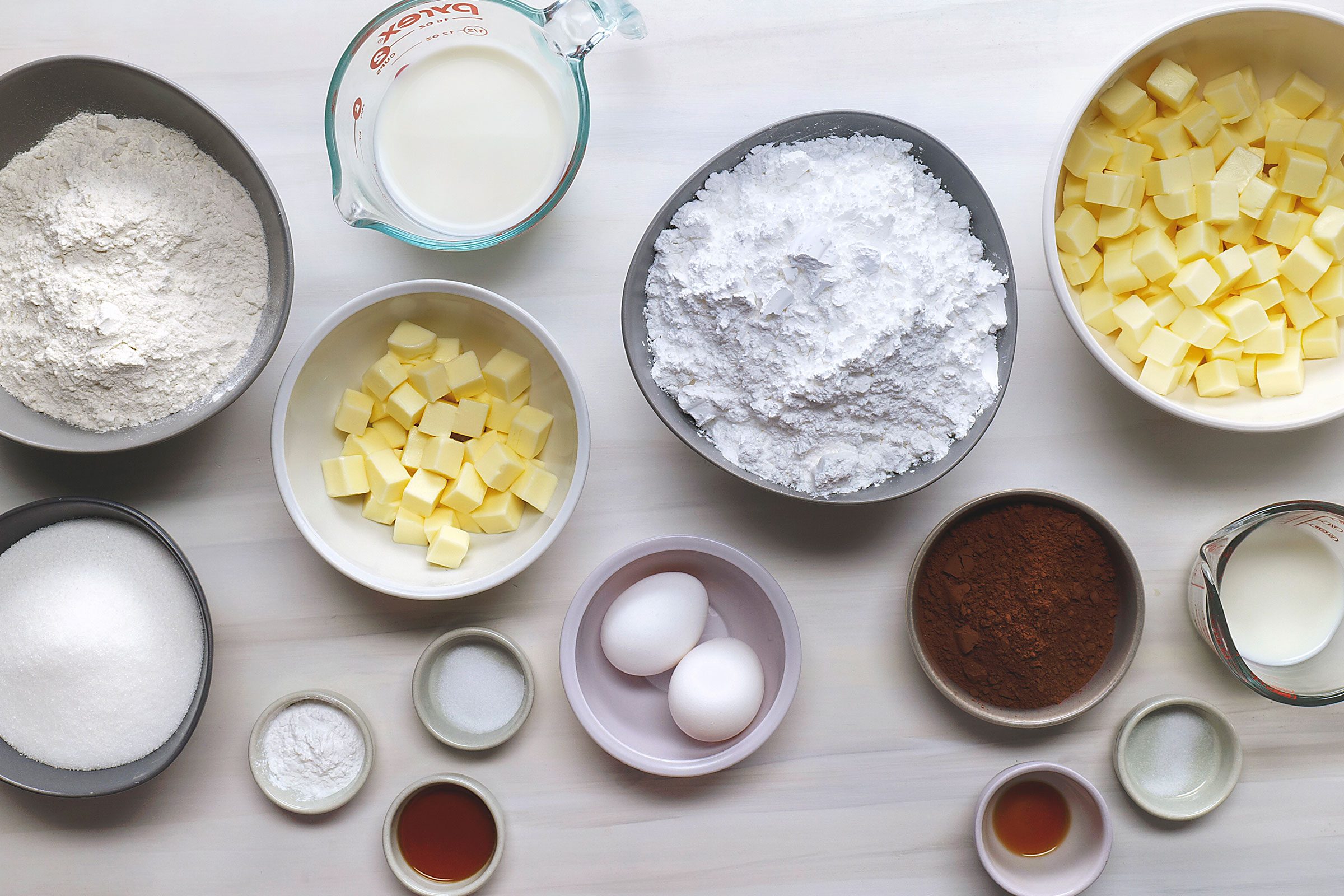 butter, sugar, eggs, vanilla extract, flour, baking powder, salt, milk, confectioners sugar, cocoa in bowls