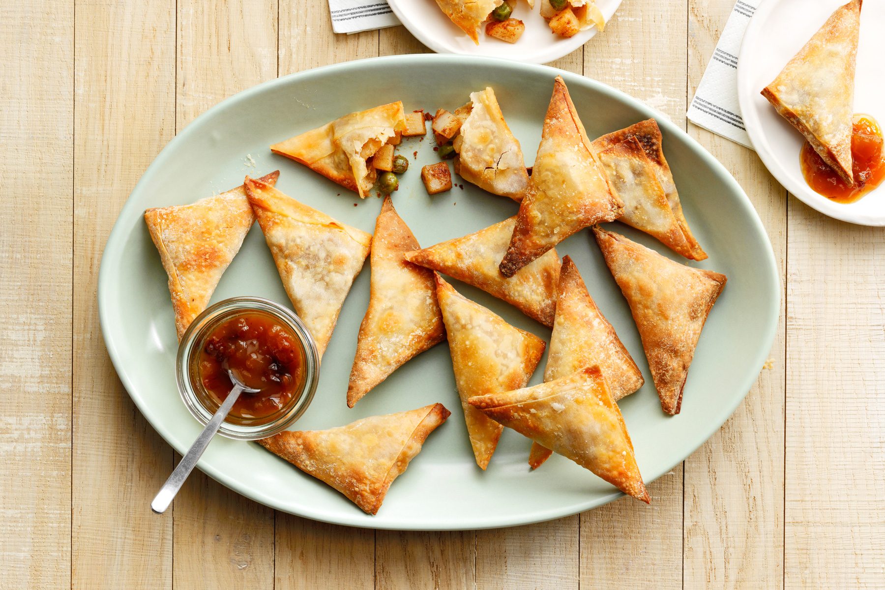 A plate of triangular Air Fryer Samosas with a small bowl of dipping sauce