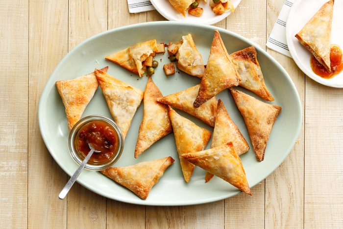 A plate of triangular Air Fryer Samosas with a small bowl of dipping sauce