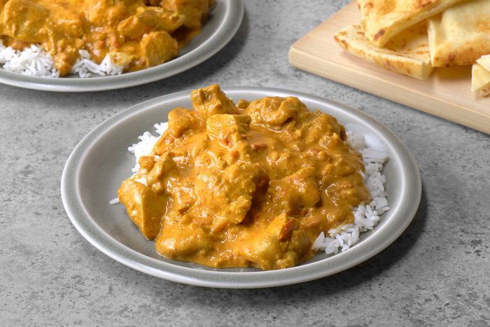 Butter chicken is elegantly served on a bed of fluffy rice, creating a colorful and inviting plate, with a side of warm naan positioned alongside. The rich sauce contrasts beautifully with the rice, promising a flavorful meal.