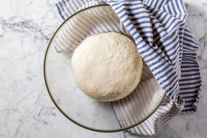 Overhead shot of placing dough in a greased bowl, turning to grease the top; covering and letting rise for 1 hour until doubled, on a marble surface with a napkin.