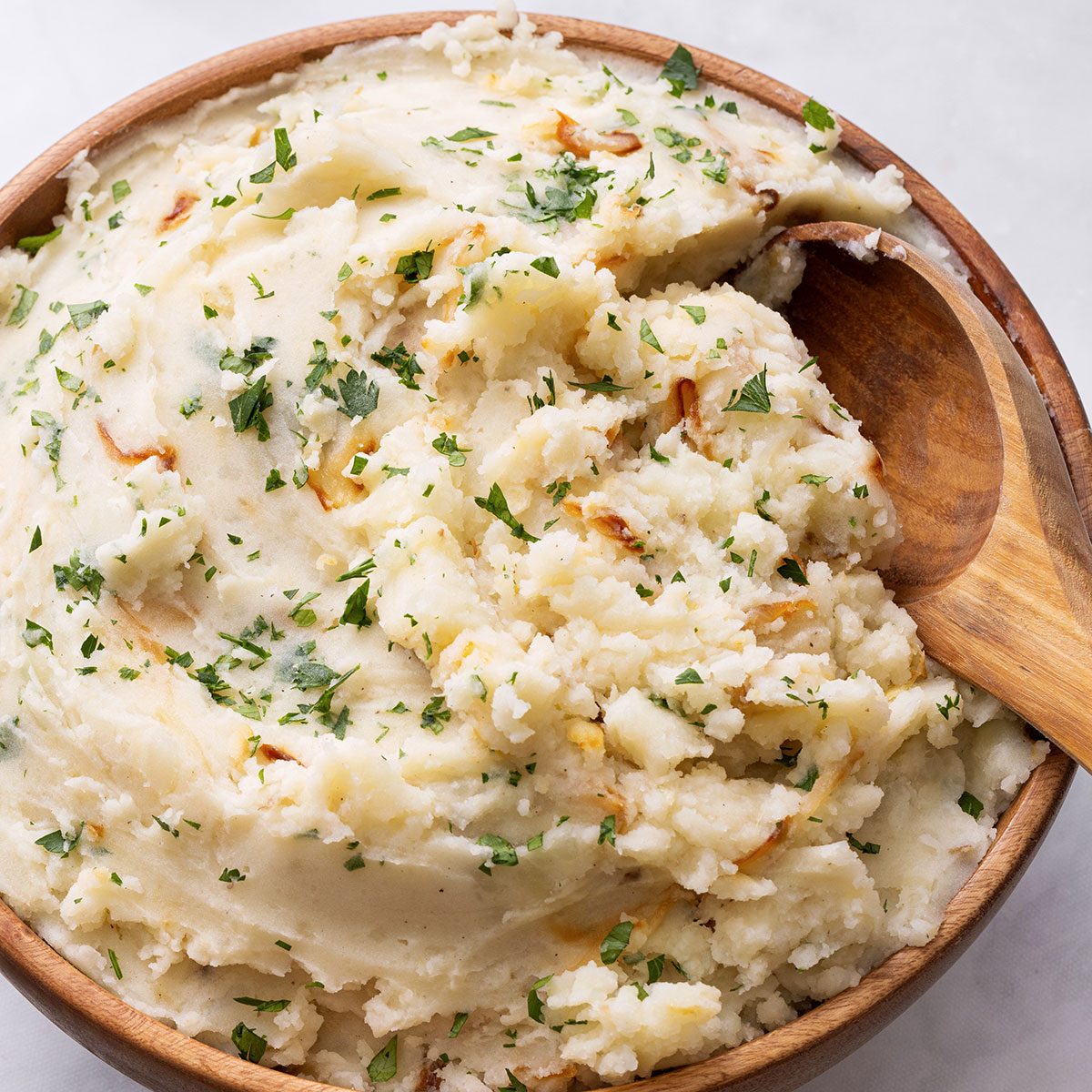 Onion Mashed Potatoes in a wooden serving bowl topped with chopped parsley for Taste of Home