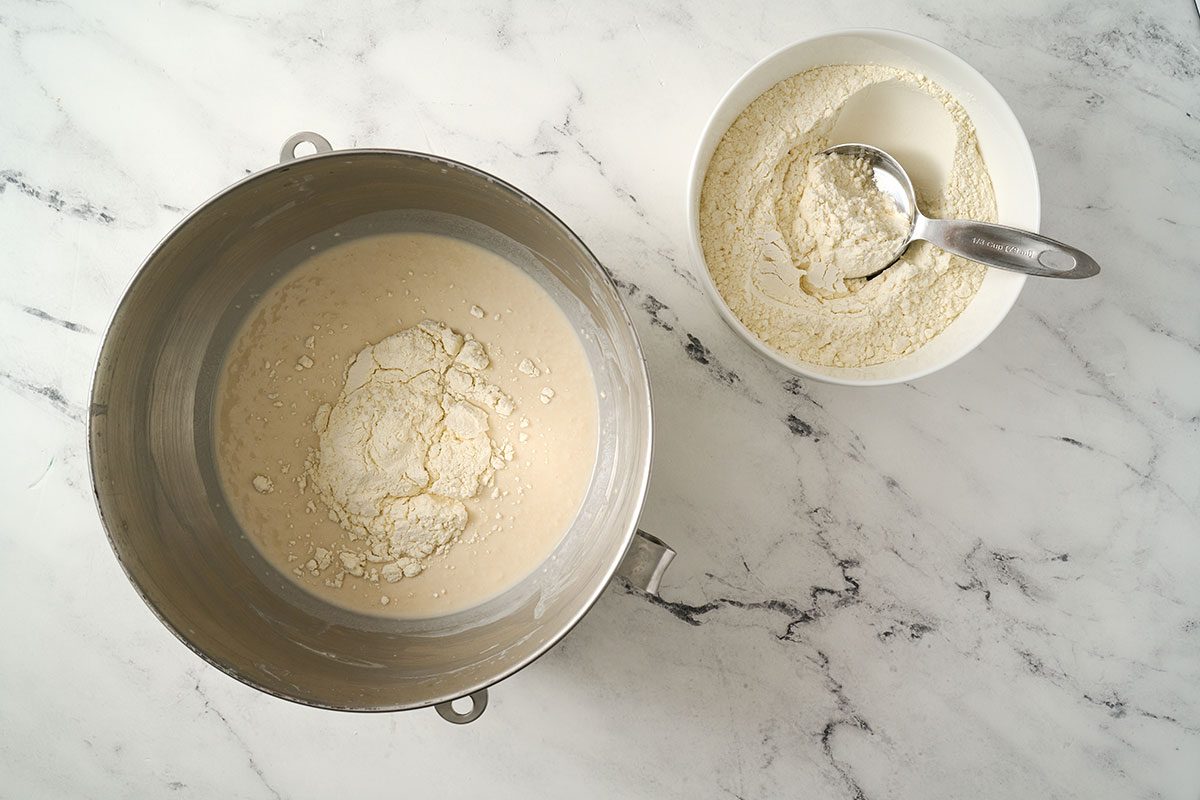 Overhead view of the remaining 3 cups of flour being stirred into the batter in a large mixing bowl, forming a stiff dough for the Taste of Home English Muffin Bread recipe.