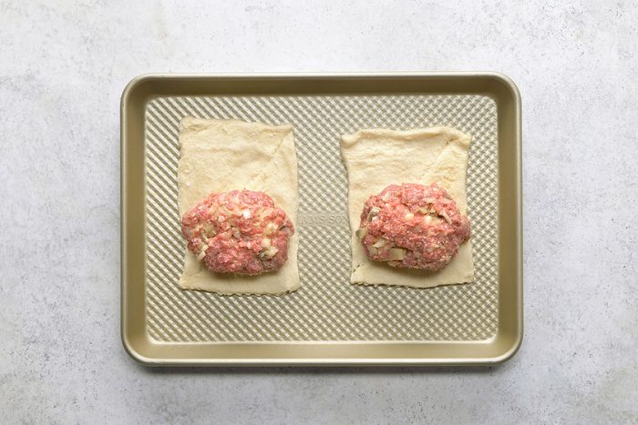 Beef and egg mixture balls separated in two halved and spread on rectangular dough sheets